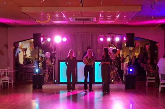 Drie mensen op een podium met kleurrijke verlichting tijdens een evenement.