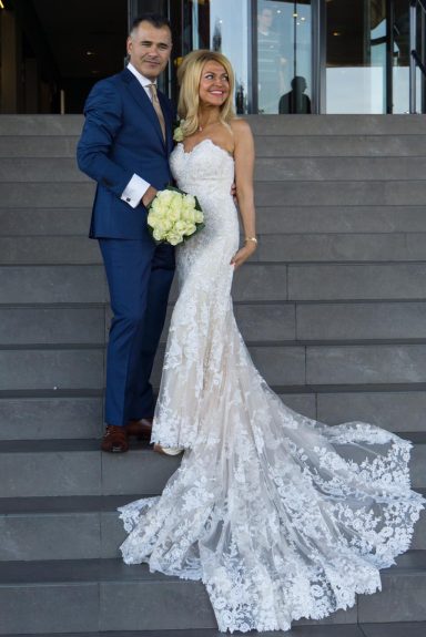 Een stel staat op een trap; de bruid draagt een mooi wit trouwjurk en de bruidegom een blauw pak.