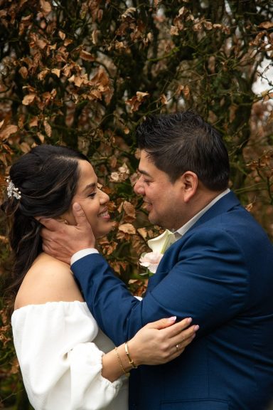 Een bruidspaar omarmt elkaar in een romantische buitenomgeving.