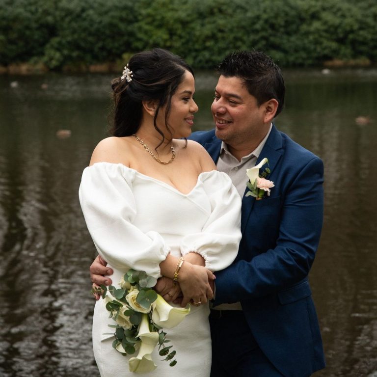 Een paar in formele kleding poseert romantisch bij een waterpartij.