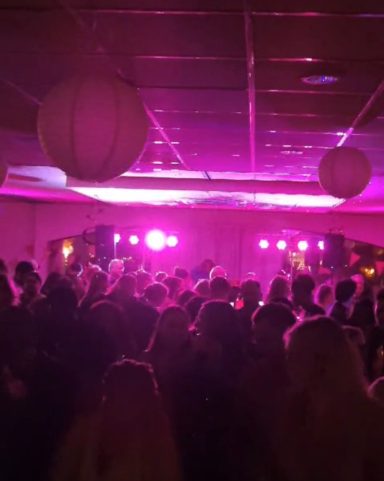 Feest met een drukke dansvloer en paarse verlichting. Hangende lampions op de achtergrond.