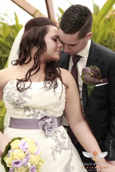 Bruid en bruidegom omhelzen elkaar in een romantische pose, omringd door bloemen.