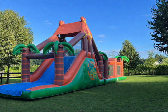 Groot opblaasbaar avontuur met glijbaan en palmboomontwerp in een groene tuin.